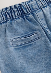 Lyseblåt denimstof med elastisk talje og en enkelt vandret baglomme med synlige syninger.