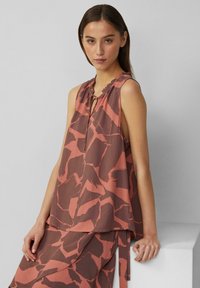Blouse sans manches dans un motif abstrait marron et corail, dotée d'un décolleté en trou de serrure avec un volant et d'une silhouette fluide.