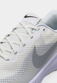 Λευκό και γκρι ανοιχτό παπούτσι Nike για τρέξιμο με υφή από δίχτυ, λευκά κορδόνια, μαύρο λογότυπο Nike στη γλώσσα και γκρι σήμα Swoosh στο πλάι.