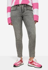 Jeans de mezclilla gris con un ajuste slim, cintura alta y textura descolorida, combinados con zapatillas rosa y blancas con diseño de cordones y suela contrastante.