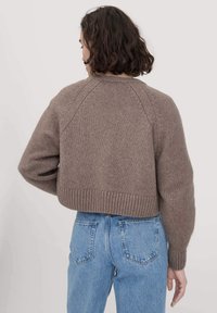 Ruskea lyhyt neule, jossa on teksturoitu neulepinta, raglan-hihat ja ribbireuna, yhdistettynä sinisiin korkeavyötäröisiin farkkuihin.