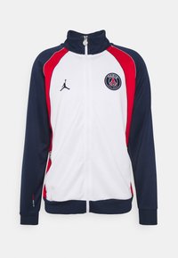 Witte jas met ritssluiting, navy mouwen en rode accenten. Voorzien van een ronde Paris-logo en een klein Jumpman-logo op de borst. Zachte stof.