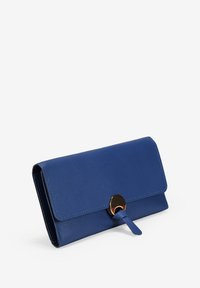 Cartera de cuero azul con una solapa asegurada por un broche redondo dorado y una correa sobre un fondo blanco.