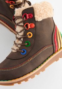 Stivali ankle in pelle marrone con un colletto peloso, occhielli multicolore e una suola texture. Presenta accenti a righe in rosso, giallo e verde.