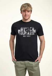 Camiseta de algodón negra con un estampado gráfico de "Star Wars" y imágenes de personajes, con "EST. 1977" en blanco, escote redondo y corte ajustado.