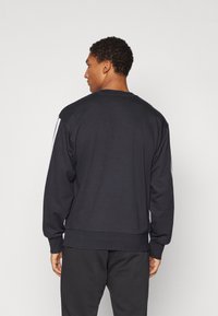 Sweatshirt preto com mangas longas, punhos e bainha ribados, apresentando detalhes brancos ao longo dos ombros. Tecido macio, corte descontraído.