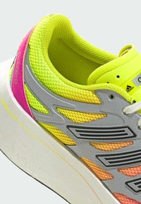Yellow and pink athletic shoe featuring a textured mesh upper, silver accents, and a thick white sole with a contrasting yellow line.