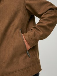 Giacca in suede marrone con tasca con zip e superficie texturizzata, dalla vestibilità rilassata e design semplice.
