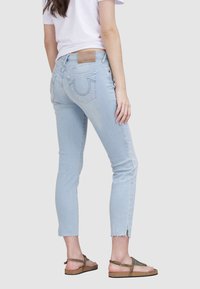 Jean bleu clair raccourci avec ourlet effiloché, comprenant deux poches arrière avec couture courbée et une étiquette en cuir de la marque sur la ceinture.