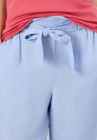 Pantalones ligeros de color azul claro, con cintura elástica y un detalle de lazo atado en la parte delantera. Textura suave con bolsillos laterales.