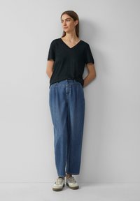 Zwarte V-hals t-shirt, relaxte pasvorm, gecombineerd met losse blauwe denim jeans. Witte en tan sneakers maken de look compleet. Eenvoudig ontwerp en texturen.