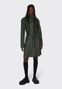 Ελιά πράσινη, αδιάβροχη με μακριά μανίκια και κουμπιά μπροστά, με κορδόνι στη μέση, και δύο πλαϊνές τσέπες. Συνδυάζεται με μαύρες κάλτσες μέχρι το γόνατο και χοντρά παπούτσια.