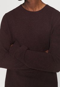Maglione in maglia borgogna con scollatura rotonda e maniche lunghe, caratterizzato da un tessuto testurizzato e una vestibilità rilassata. Senza loghi o motivi visibili.