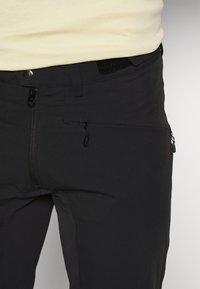 Crne tehničke hlače s prednjim džepom na zip, podesivim pojasom s čičak trakom i elegantnim, aerodinamičnim dizajnom.