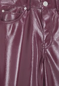 Gros plan d’un pantalon en cuir verni bordeaux brillant montrant la poche avant, la boucle de ceinture, le bouton et les détails de la fermeture éclair.