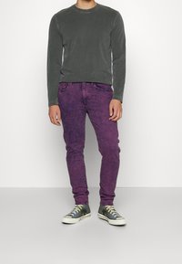 Grå långärmad skjorta med rund hals, kombinerad med lila, slitna skinny jeans och grå sneakers med vita sulor och gröna snören.