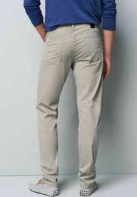 Lichtbeige broek met een slim fit, achterzakken en een gladde textuur, gecombineerd met grijze schoenen, vanachter bekeken.