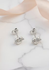 Boucles d'oreilles en argent en forme de nœud, avec une finition lisse et polie et un design simple. Fixées avec des fermoirs papillon classiques.