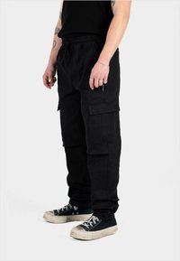 Pantaloni cargo negri cu un croi lejer, talie elastică și multiple buzunare. Purtați cu teniși negri și gri cu talpă înaltă.