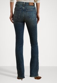 Mørkeblå flarejeans med høy midje, laget av denim. Har to baklommer og et lærmerke i livet.
