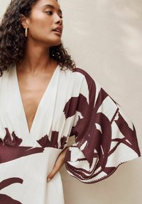 Langes, tiefes V-Ausschnittkleid in Creme mit kastanienbraunen abstrakten Blumenmustern. Verfügt über schwingende Ärmel und eine taillierte Taille für eine fließende Silhouette.