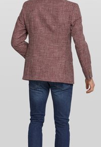 Blazer bordeaux con texture, dotato di uno spacco posteriore e polsini a tre bottoni, abbinato a jeans in denim scuro. Il tessuto presenta un sottile motivo a trama.