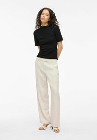 Maglietta nera a maniche corte con texture abbinata a pantaloni larghi crema e sandali aperti crema, che mostrano un fit rilassato e un design semplice.
