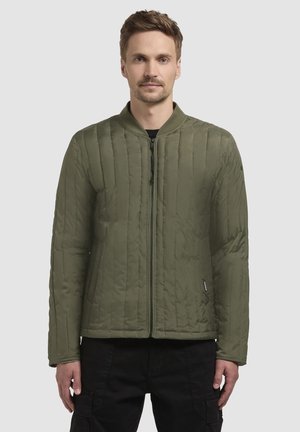 Oliven grøn quiltet bomberjakke med ribbet krave, frontlynlås og sidelommer. Stoffet er glat med en mat finish.