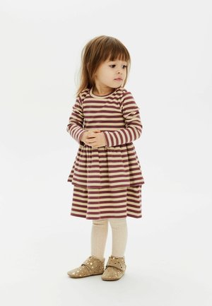Gestreiftes Kleid in Kastanienbraun und Beige, geschichtetes Design, lange Ärmel, kombiniert mit kremfarbener Strumpfhose und goldgepunkteten Schuhen.
