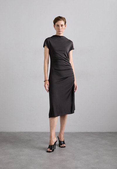 Dark gray, knee-length dress with short sleeves and a high neckline, featuring side ruching. Worn with open-toe black heeled sandals.