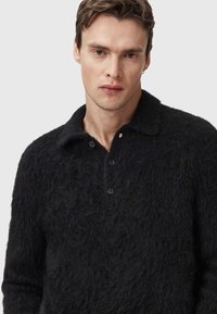 Suéter negro de punto difuso con cuello, tres botones y una superficie texturizada, que presenta un corte relajado y mangas largas.