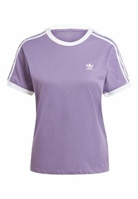 Lila bomulls t-shirt med vit kant, korta ärmar och tre vita ränder längs axlarna. Har en liten vit logotyp på bröstet.