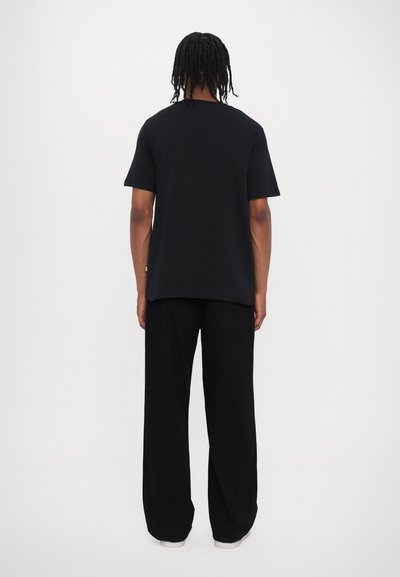 T-shirt negru cu mânecă scurtă, cu o croială lejeră, asociat cu pantaloni negri largi, ambele realizate dintr-un material moale, văzute din spate.