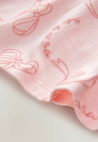 Tessuto di cotone color rosa chiaro con sottili motivi ricamati di scarpette da balletto e nastri. Texture liscia con un leggero dettaglio arricciato sul bordo.