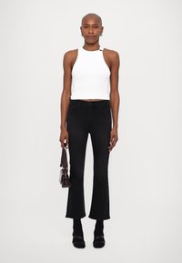 Top alb, scurt, cu gât halter, blugi negri cu talie înaltă, evazați, botine negre cu toc, și o poșetă mică maro. Texturi fine, design minimalist.