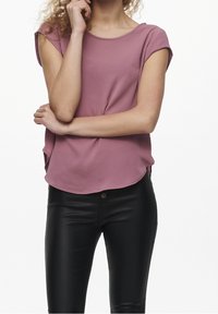Top rosa a maniche corte con collo rotondo, orlo curvo e finitura testurizzata, abbinato a pantaloni neri aderenti con chiusura a bottone.