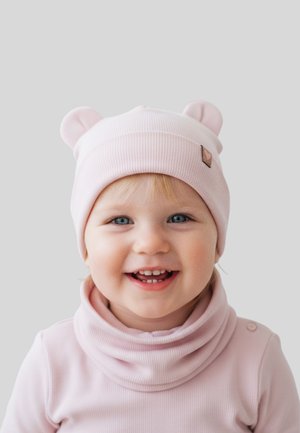 Rosa gerippte Mütze mit Bärenohren und kleinem Herz-Logo. Kind trägt einen passenden Rollkragenpullover, zeigt hellblondes Haar und blaue Augen.