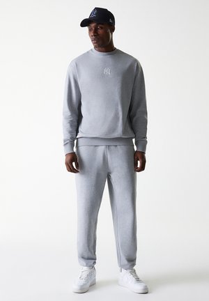 Gray sweatshirt and sweatpants set in soft fabric with ribbed cuffs, paired with a black baseball cap featuring a logo and white sneakers.