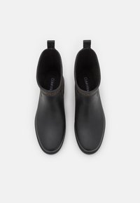 Une paire de bottes noires à cheville avec des tirettes et un bord à motifs marron, vue de dessus sur un fond blanc.