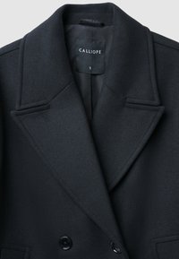 Cappotto in lana nera con design doppiopetto, rever a punta e due tasche frontali. Presenta un interno liscio e un'etichetta contrassegnata "CALLIOPE".