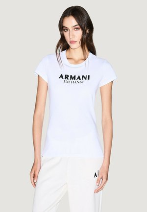 T-shirt blanc en coton à manches courtes, présentant un logo noir "ARMANI EXCHANGE" sur la poitrine. Design ajusté et col ras du cou.