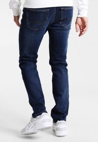 Mörkblå denimjeans med smal passform, som har två bakfickor med kontrasterande sömmar och en lätt blekning. Bärs med vita sneakers.
