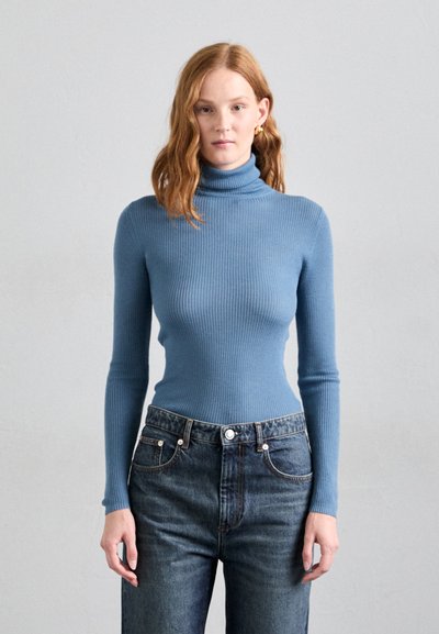 Geribbelde coltrui in lichtblauw, aansluitend ontwerp met lange mouwen, gecombineerd met hoog-waist donkere denim jeans met voorzakken.