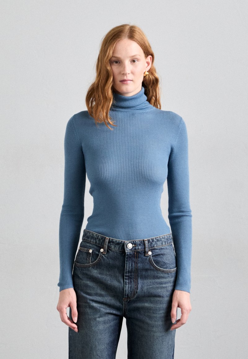 Ribbed turtleneck sweater in light blue, fitted design with long sleeves, paired with high-waisted dark denim jeans, featuring front pockets.