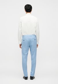 Pantalon bleu clair confectionné dans un tissu texturé, à coupe droite avec deux poches arrière. Porté avec une chemise blanche à boutons.