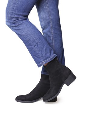 Bottines en suède noir avec un bout rond et un petit talon carré, associées à un jean en denim bleu ajusté, illustrant un style décontracté.