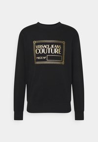 Svart sweatshirt med lång ärm och guld "Versace Jeans Couture"-logotyp samt dekorerande ram på bröstet, tomt utrymme för stycknummer.