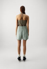 Top bez ramínek s nařasením v olivové barvě, v kombinaci se světle zelenými šortkami s pružným pasem. Oblečeno s černými vysokými teniskami a ponožkami.