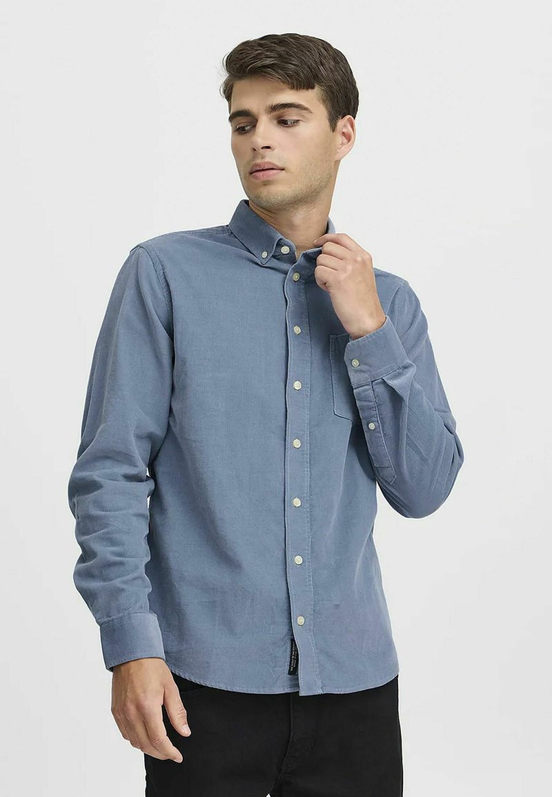 Himmelblaues Button-up-Hemd aus Baumwolle, mit Kragen, langen Ärmeln und einer Brusttasche. Subtile Textur mit kleinen Knöpfen.