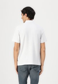 Hvid kortærmet polo skjorte med struktureret stof, flad krave og en sideslids i kanten, parret med grå denim jeans.